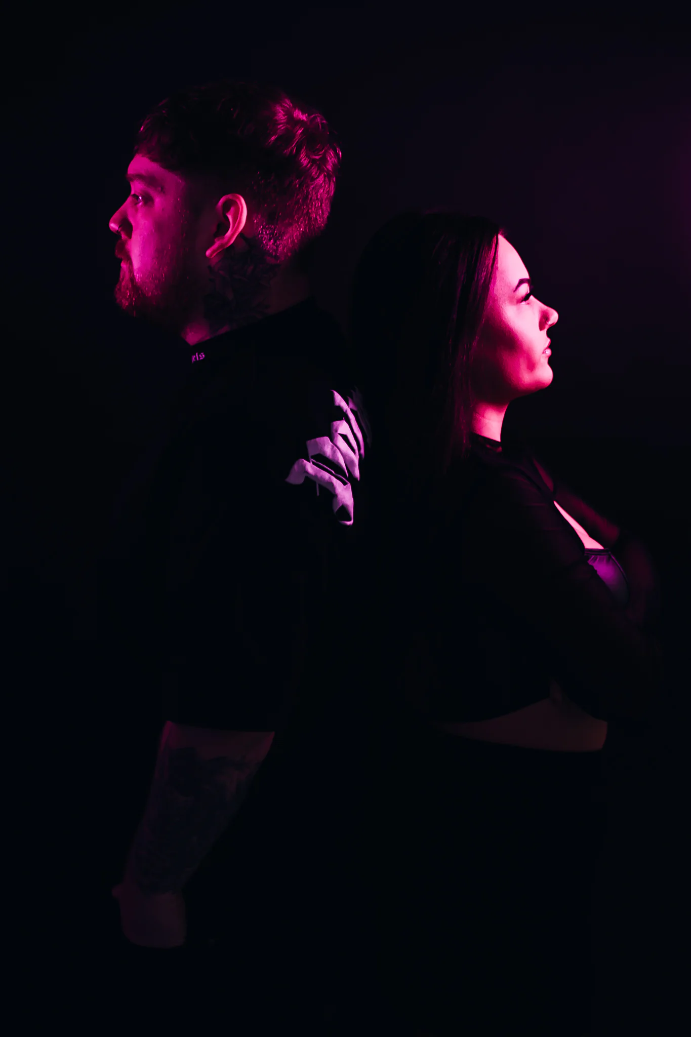 Jamie & Britney of Moodswing standing back to back in a magenta-lit studio portrait
